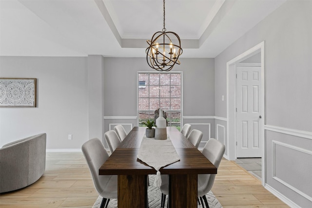 dining room with a chandelier, a raised ceiling, and light wood finished floors