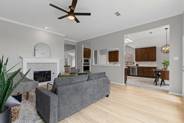 living area with a ceiling fan, a glass covered fireplace, ornamental molding, baseboards, and light wood-style floors
