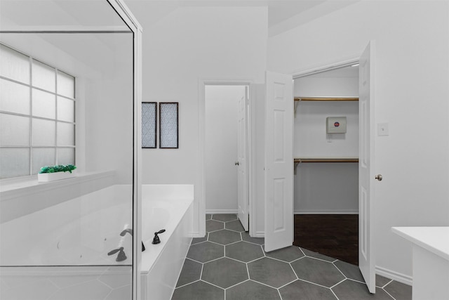 bathroom featuring a garden tub, a spacious closet, and tile patterned floors