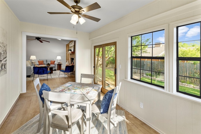 dining room featuring a ceiling fan, light wood-type flooring, and a brick fireplace