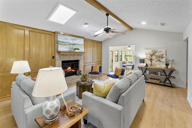 living area featuring a brick fireplace, light wood finished floors, ceiling fan, a textured ceiling, and baseboards