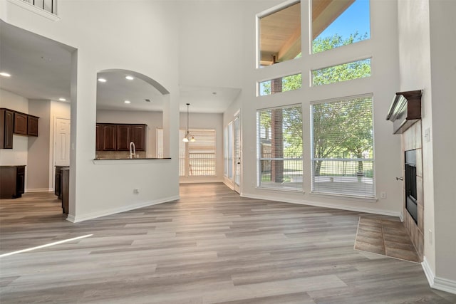 10101 Waterview Pkwy, Rowlett, TX 75089 - unfurnished living room with a glass covered fireplace, a towering ceiling, baseboards, light wood-style floors, and arched walkways