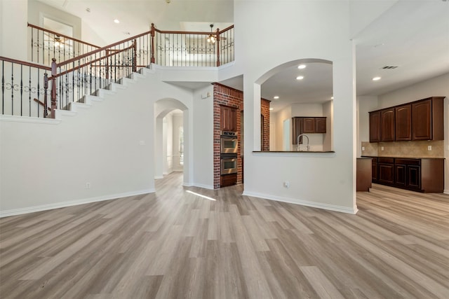 10101 Waterview Pkwy, Rowlett, TX 75089 - unfurnished living room featuring light wood finished floors, arched walkways, a towering ceiling, stairway, and baseboards