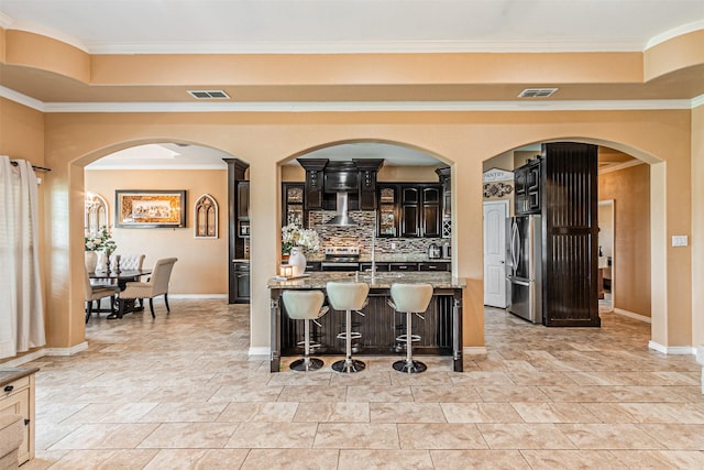 kitchen featuring appliances with stainless steel finishes, a breakfast bar area, decorative backsplash, ornamental molding, and light stone counters