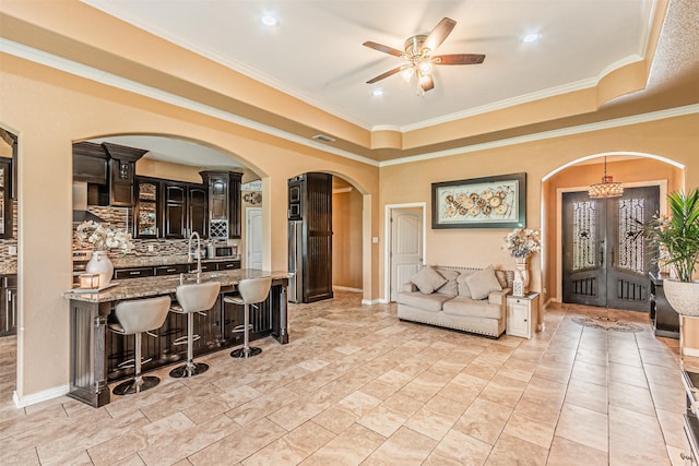 living area featuring arched walkways, ceiling fan, crown molding, a raised ceiling, and baseboards