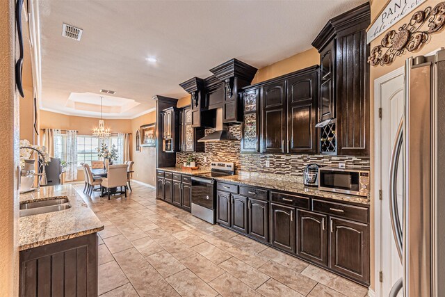 kitchen featuring stainless steel appliances, backsplash, a raised ceiling, a chandelier, and a sink
