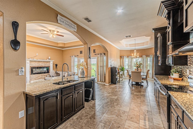 kitchen featuring a tray ceiling, a sink, range with electric cooktop, arched walkways, and a chandelier