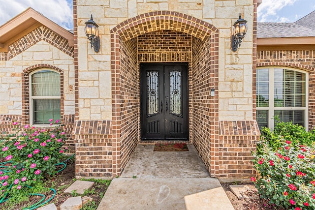 view of exterior entry with french doors, brick siding, and stone siding