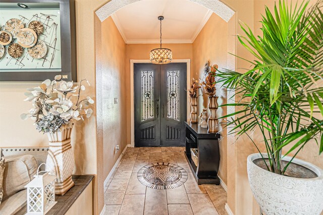 tiled entrance foyer featuring arched walkways, crown molding, a chandelier, a textured wall, and baseboards