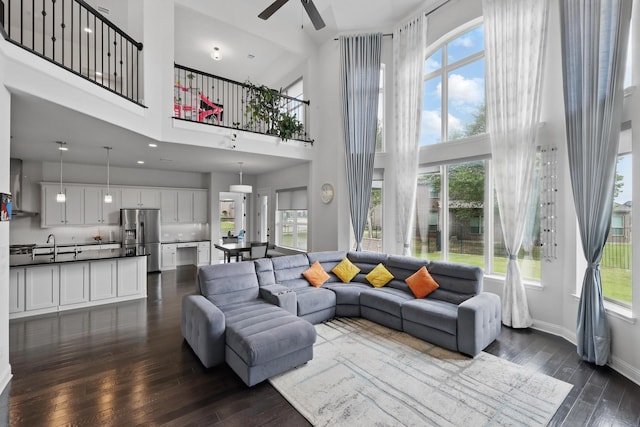 living room featuring ceiling fan, healthy amount of natural light, dark wood-style flooring, and a towering ceiling