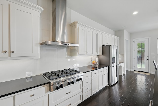 kitchen with wall chimney range hood, stainless steel appliances, dark countertops, dark wood-style flooring, and white cabinetry