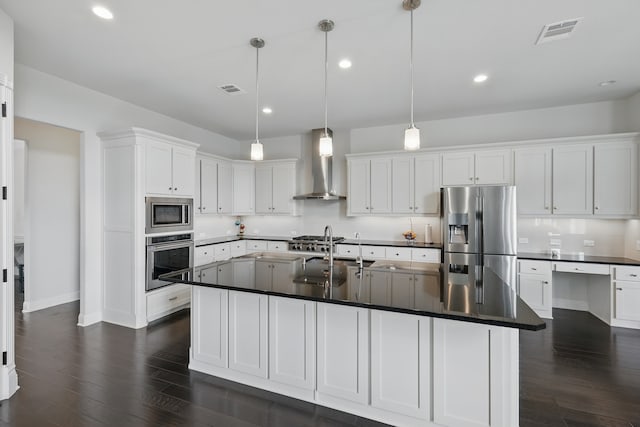 kitchen featuring stainless steel appliances, wall chimney range hood, a sink, dark countertops, and recessed lighting