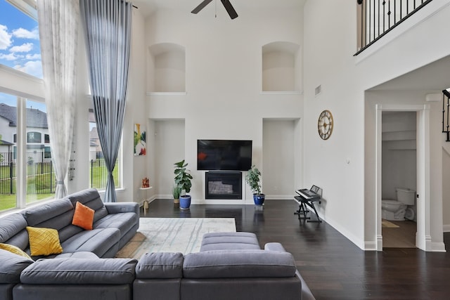 living room with ceiling fan, a towering ceiling, dark wood-style floors, and baseboards