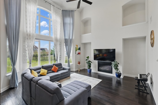 living area featuring a high ceiling, plenty of natural light, a ceiling fan, baseboards, and dark wood finished floors