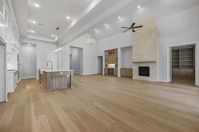 4316 Sandbrock Pkwy, Aubrey, TX 76227 - kitchen featuring a towering ceiling, a ceiling fan, a chandelier, a fireplace, and light wood-style floors