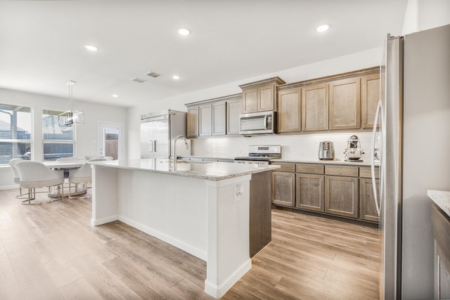 628 Hidden Cove Dr, Princeton, TX 75407 - kitchen featuring stainless steel appliances, a center island with sink, light wood-type flooring, a sink, and light stone counters