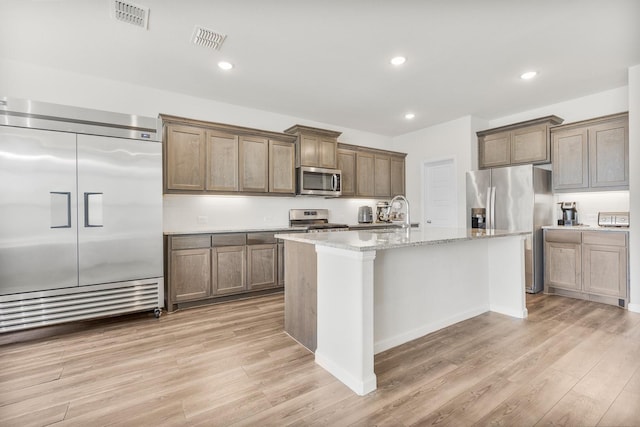 628 Hidden Cove Dr, Princeton, TX 75407 - kitchen with stainless steel appliances, light wood-style floors, an island with sink, light stone countertops, and recessed lighting