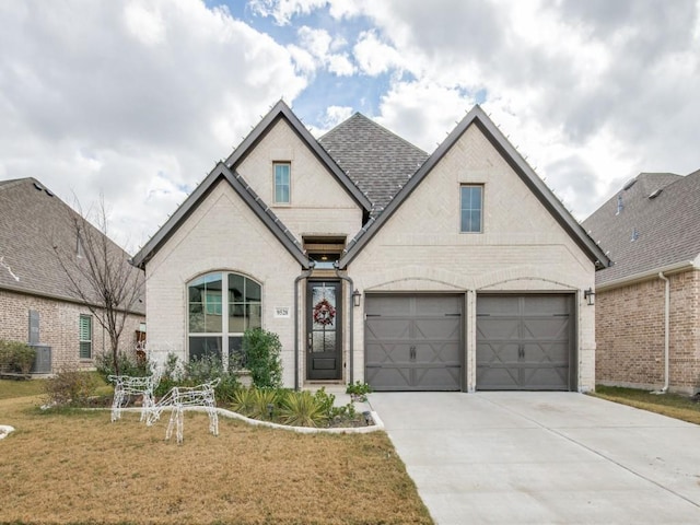 french country home featuring brick siding, concrete driveway, a garage, and a front yard