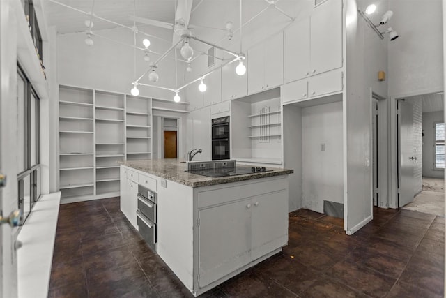 kitchen with open shelves, a towering ceiling, black appliances, white cabinetry, and a center island with sink