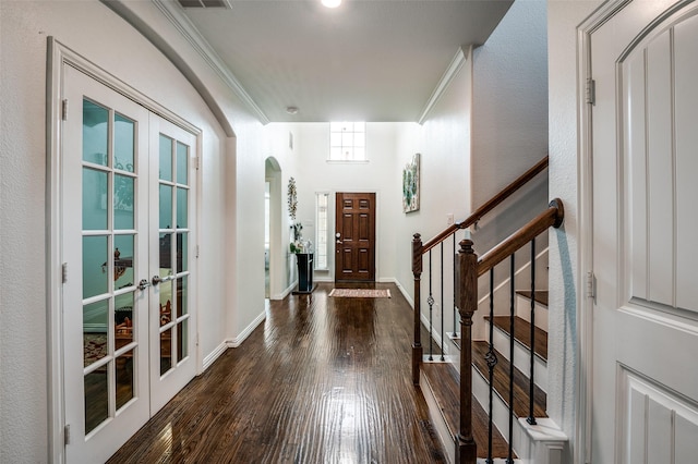 foyer featuring wood finished floors, french doors, crown molding, arched walkways, and stairs