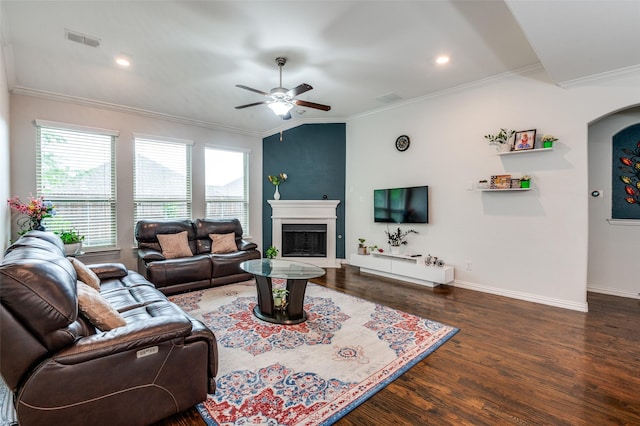living room with a ceiling fan, wood finished floors, baseboards, a fireplace with raised hearth, and crown molding