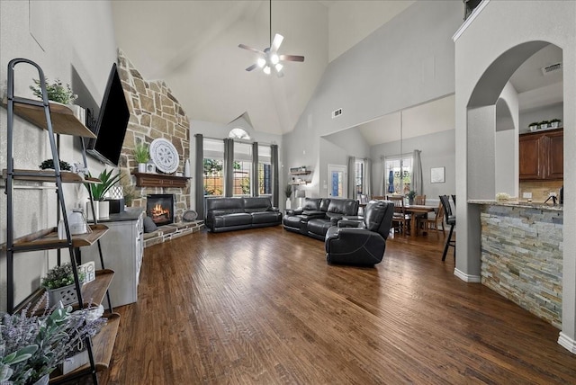 living room with high vaulted ceiling, a ceiling fan, a stone fireplace, dark wood finished floors, and arched walkways