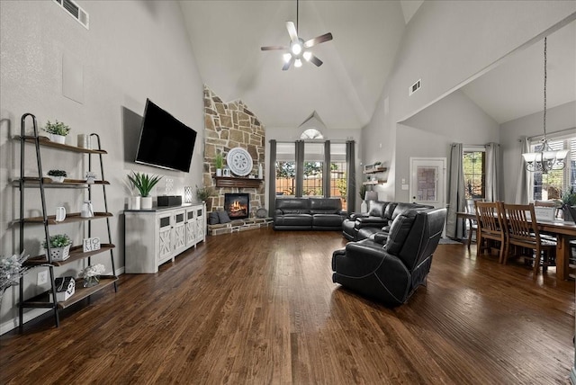 living area featuring high vaulted ceiling, a ceiling fan, dark wood finished floors, a stone fireplace, and a chandelier