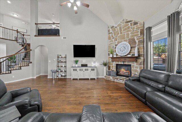 living area featuring a ceiling fan, stairs, a stone fireplace, wood finished floors, and high vaulted ceiling