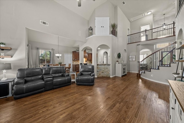living room with arched walkways, dark wood-style floors, high vaulted ceiling, a chandelier, and stairway