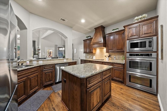 kitchen with stainless steel appliances, custom range hood, a sink, a center island, and dark wood-style flooring