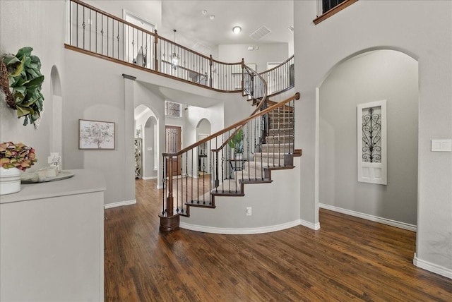 foyer entrance featuring arched walkways, wood finished floors, a towering ceiling, baseboards, and stairway