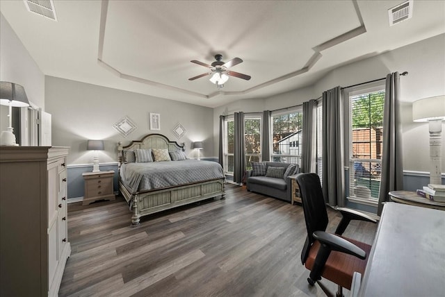 bedroom featuring a tray ceiling, dark wood-style flooring, baseboards, and ceiling fan