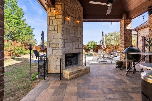 view of patio with an outdoor stone fireplace, a fenced backyard, a ceiling fan, and outdoor dining area
