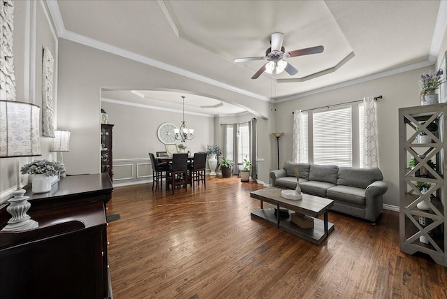 living room featuring arched walkways, a raised ceiling, a ceiling fan, wood finished floors, and a chandelier