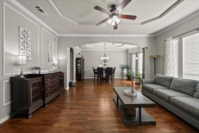 living room featuring arched walkways, a raised ceiling, a ceiling fan, dark wood-style floors, and crown molding
