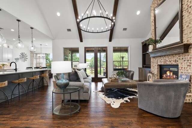 living room featuring dark wood-style floors, plenty of natural light, beam ceiling, a chandelier, and a fireplace