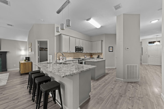 4719 Highlands Dr, Mckinney, TX 75070 - kitchen with stainless steel appliances, a sink, light wood finished floors, light stone countertops, and a peninsula