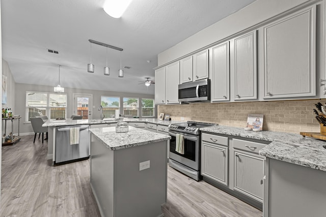 4719 Highlands Dr, Mckinney, TX 75070 - kitchen with appliances with stainless steel finishes, gray cabinetry, a peninsula, light wood-style flooring, and backsplash