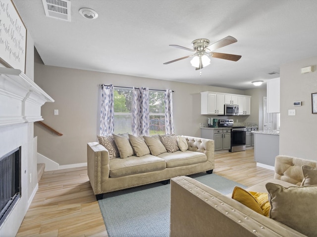 living area featuring light wood-style flooring, a ceiling fan, a fireplace, and baseboards