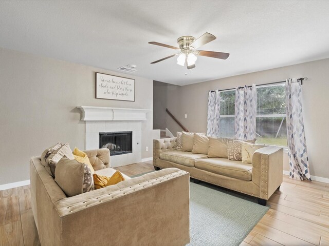 living area with light wood finished floors, baseboards, a ceiling fan, and a tiled fireplace
