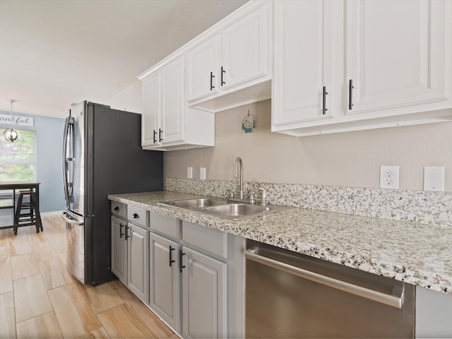 kitchen with stainless steel appliances, a sink, white cabinets, and light stone counters