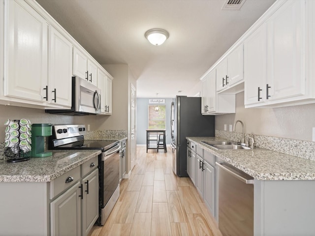 kitchen with appliances with stainless steel finishes, a sink, gray cabinets, white cabinets, and baseboards