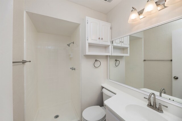 bathroom featuring toilet, a tile shower, and vanity