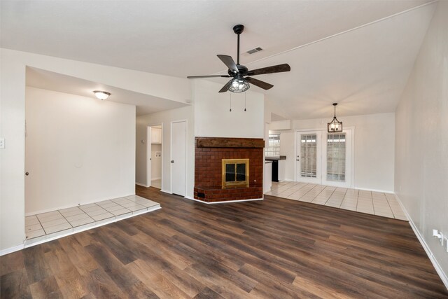 unfurnished living room with wood finished floors, vaulted ceiling, ceiling fan, baseboards, and a brick fireplace