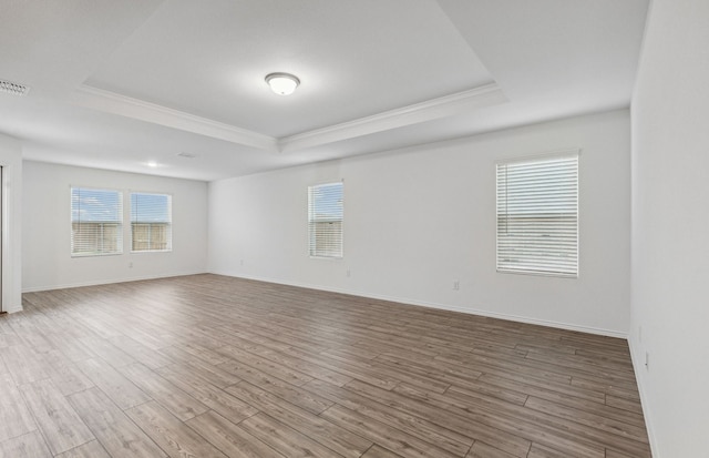 empty room featuring a raised ceiling, crown molding, wood finished floors, and baseboards