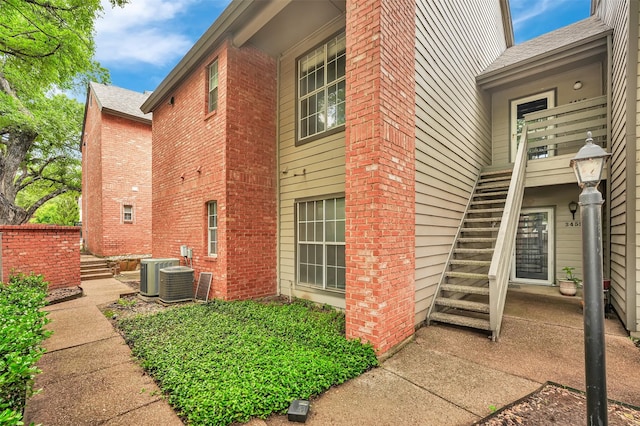 view of home's exterior featuring stairs, brick siding, and central AC unit