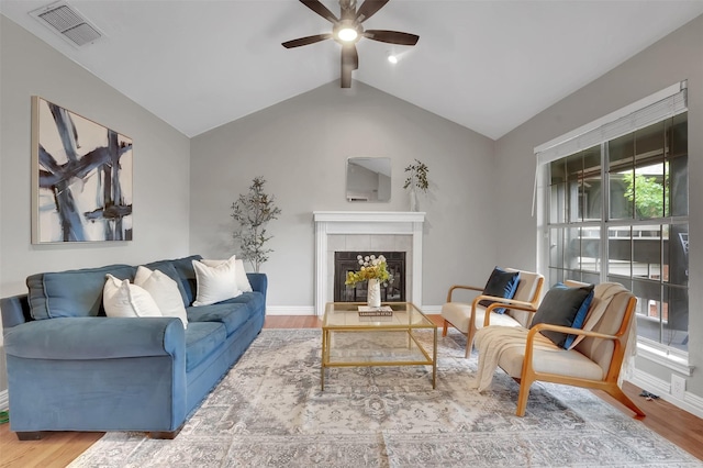 living room featuring ceiling fan, wood finished floors, a tile fireplace, and baseboards