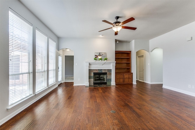 unfurnished living room with a ceiling fan, a fireplace, baseboards, and arched walkways