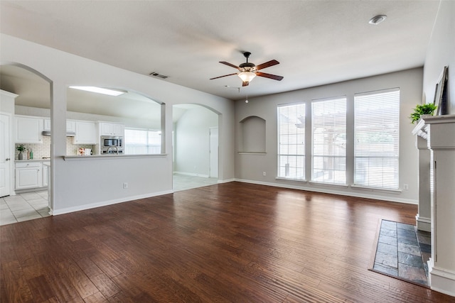unfurnished living room with a ceiling fan, light wood finished floors, healthy amount of natural light, and arched walkways