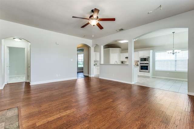 unfurnished living room featuring a ceiling fan, healthy amount of natural light, light wood-type flooring, and a chandelier